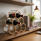Geometric gold wine rack holding bottles on a wooden shelf with books and a plant.