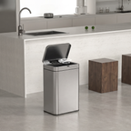 A stainless steel canless trash can with its lid open, placed on a light gray tiled floor next to a white kitchen island.